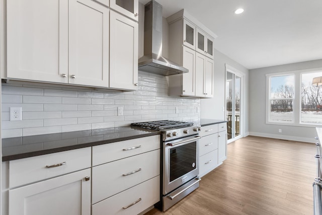 kitchen featuring dark countertops, wall chimney range hood, tasteful backsplash, and high end range