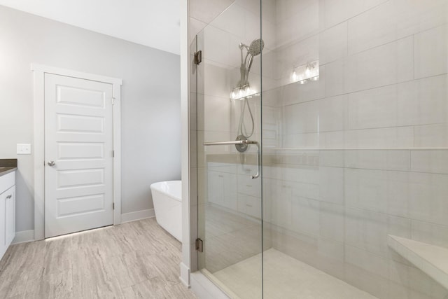 full bathroom with baseboards, wood finished floors, a freestanding bath, vanity, and a shower stall