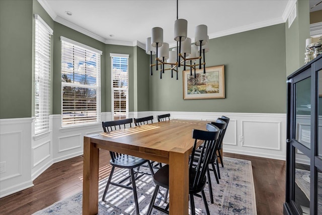 dining space featuring dark wood-type flooring, a wainscoted wall, crown molding, and an inviting chandelier