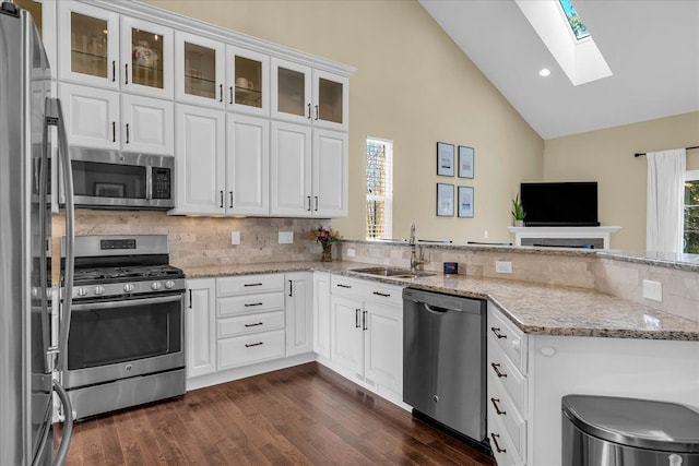 kitchen with vaulted ceiling with skylight, dark wood-type flooring, a sink, white cabinets, and appliances with stainless steel finishes