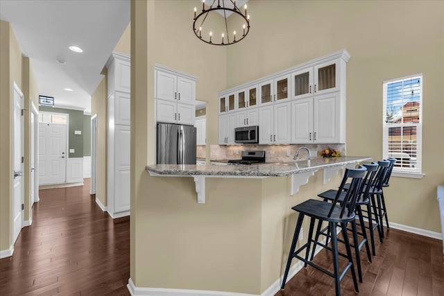 kitchen featuring tasteful backsplash, dark wood finished floors, appliances with stainless steel finishes, light stone counters, and a peninsula