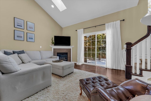 living room featuring a skylight, a glass covered fireplace, wood finished floors, stairs, and high vaulted ceiling