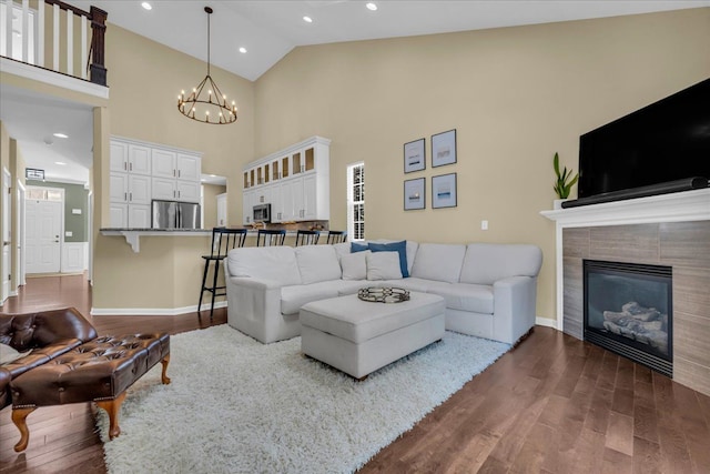 living area with a tile fireplace, dark wood finished floors, baseboards, and an inviting chandelier