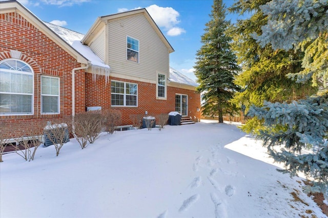 snow covered property featuring entry steps and brick siding