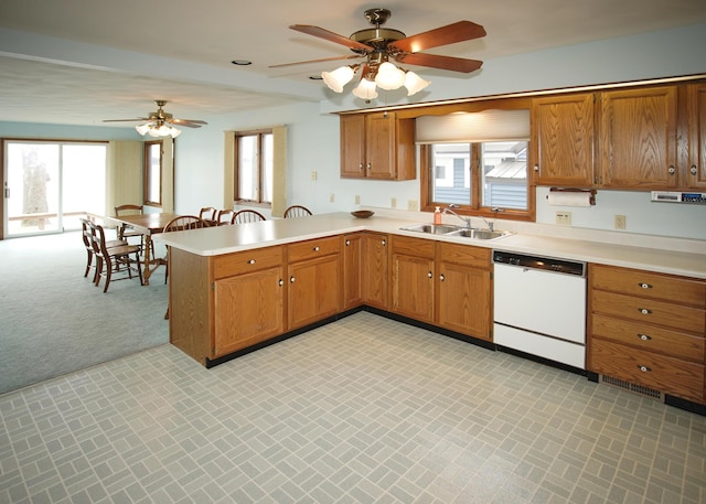 kitchen featuring a peninsula, white dishwasher, brown cabinetry, and a sink