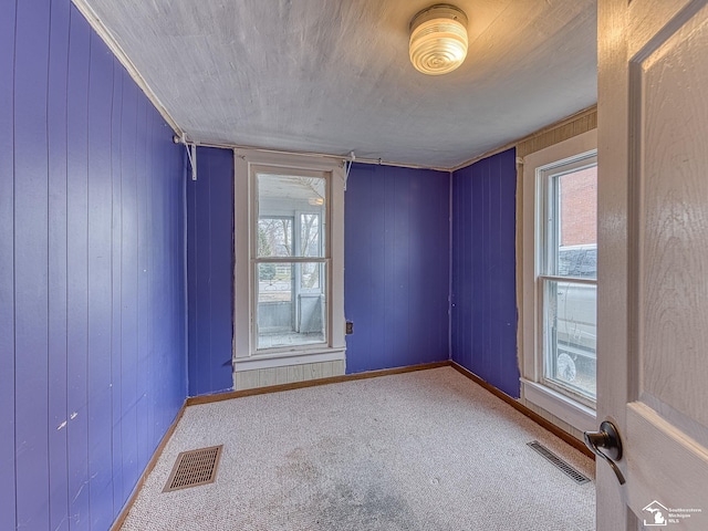 carpeted empty room with baseboards, wooden walls, and visible vents