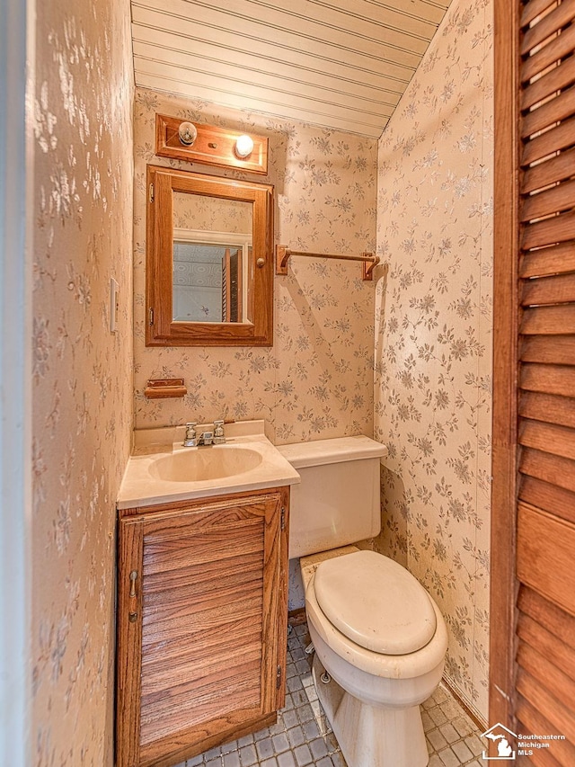 half bathroom featuring vanity, toilet, and wallpapered walls