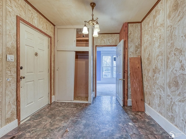 foyer entrance featuring crown molding, an inviting chandelier, stone finish flooring, baseboards, and wallpapered walls