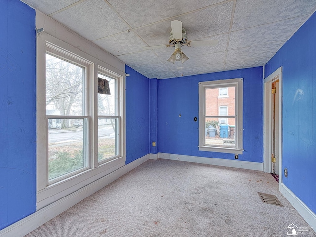 carpeted empty room featuring a paneled ceiling, baseboards, visible vents, and ceiling fan