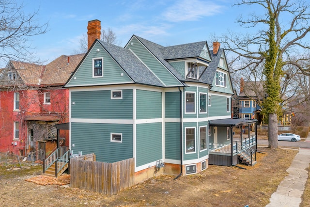 view of side of property with roof with shingles, a porch, a chimney, and fence