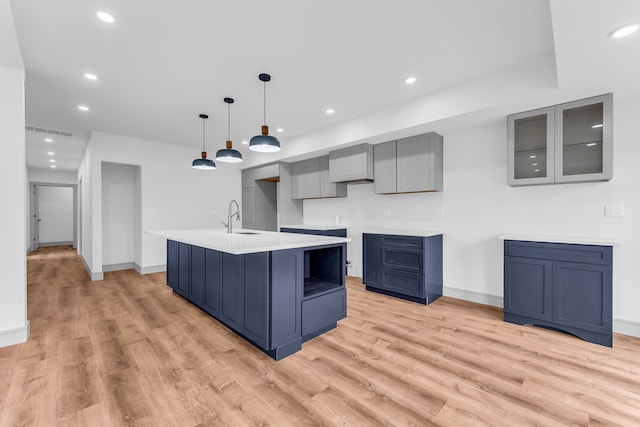 kitchen with light wood-style floors, a kitchen island with sink, a sink, and recessed lighting