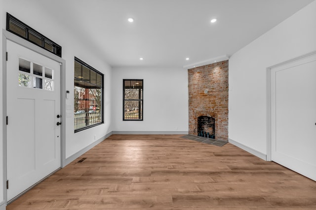 foyer entrance featuring recessed lighting, a fireplace, visible vents, baseboards, and light wood-style floors