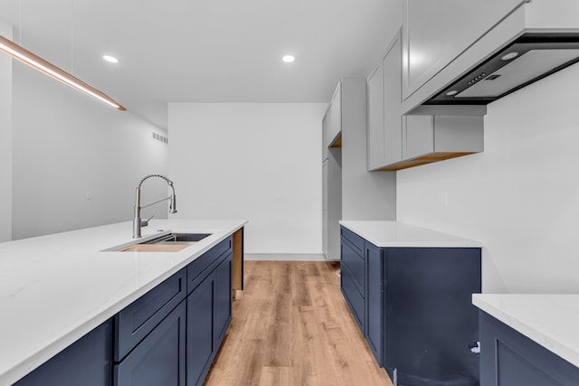 kitchen featuring light wood finished floors, blue cabinetry, a sink, and visible vents