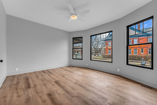 empty room with a ceiling fan, baseboards, visible vents, and wood finished floors