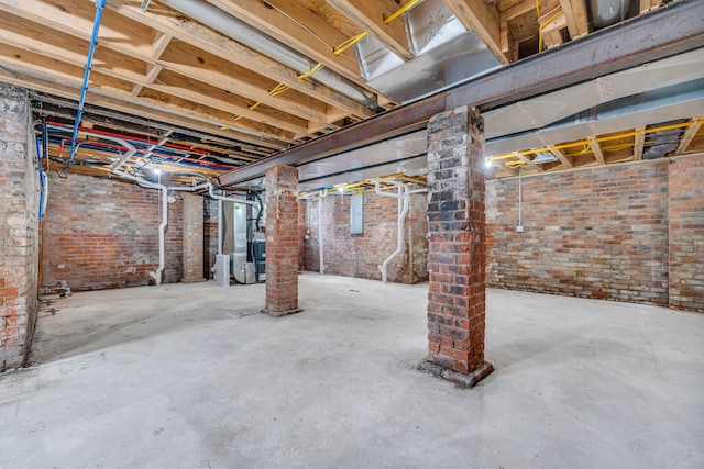 unfinished below grade area with heating unit, electric panel, and brick wall