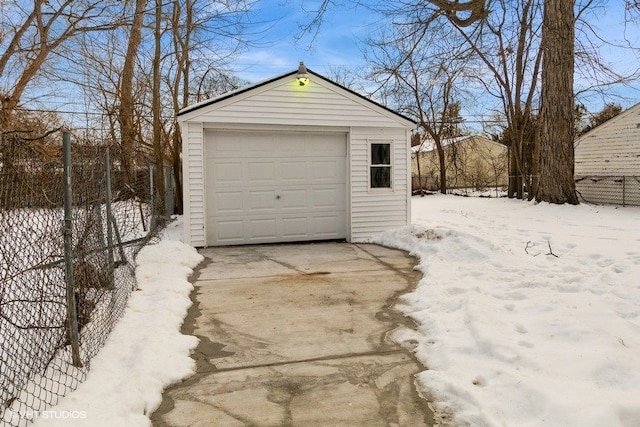 snow covered garage with concrete driveway, a detached garage, and fence