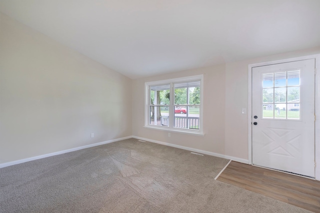 doorway to outside with lofted ceiling, visible vents, baseboards, and carpet flooring