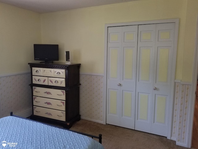 carpeted bedroom with a wainscoted wall, a closet, and wallpapered walls