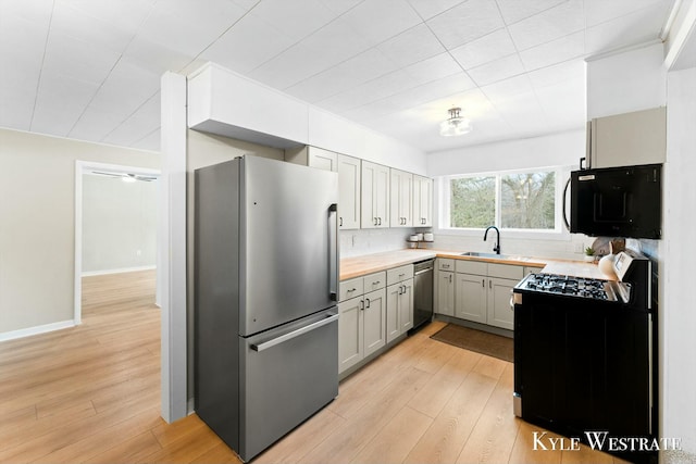 kitchen with baseboards, appliances with stainless steel finishes, light countertops, light wood-style floors, and a sink