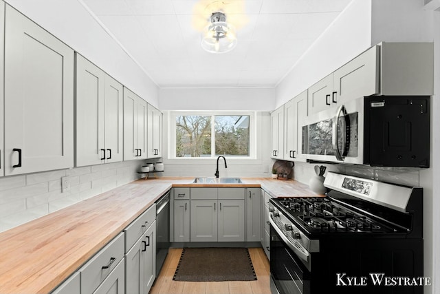 kitchen with tasteful backsplash, appliances with stainless steel finishes, gray cabinetry, wooden counters, and a sink