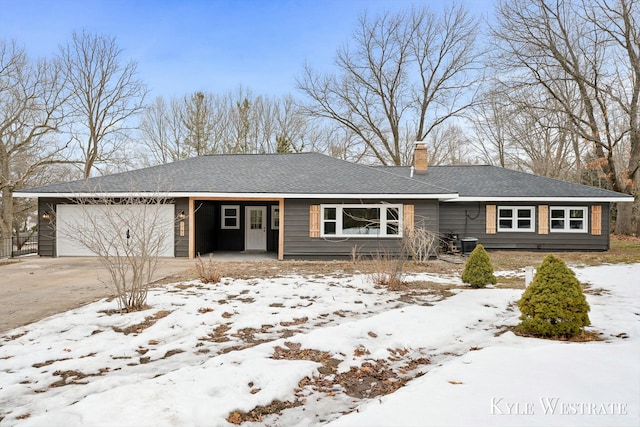 ranch-style house with a chimney, a shingled roof, central AC unit, a garage, and driveway