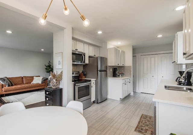 kitchen featuring decorative backsplash, appliances with stainless steel finishes, open floor plan, light countertops, and a sink