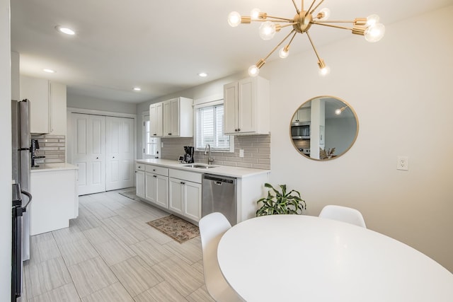 kitchen with light countertops, freestanding refrigerator, white cabinets, a sink, and dishwasher