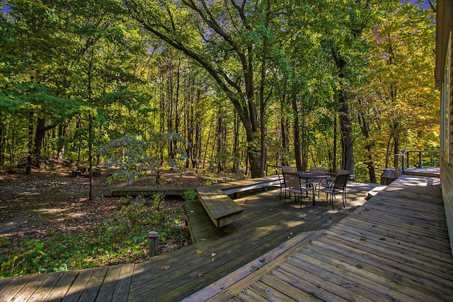 deck with a forest view and outdoor dining space