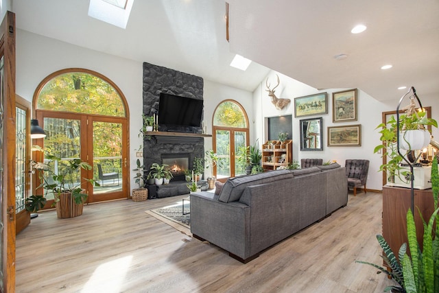 living area with high vaulted ceiling, a skylight, a fireplace, french doors, and light wood-type flooring