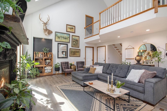 living area with a fireplace, stairway, a towering ceiling, and wood finished floors