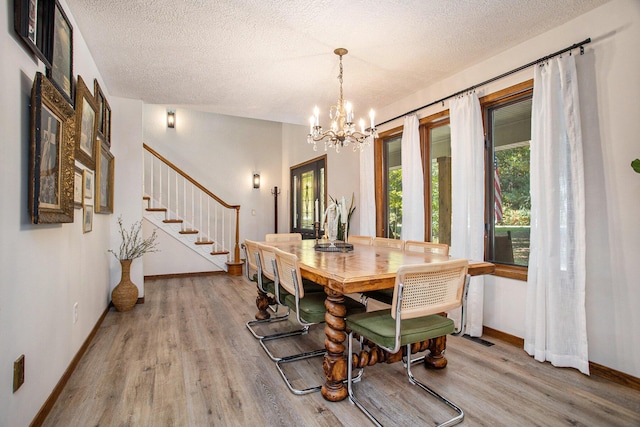 dining room featuring an inviting chandelier, a textured ceiling, wood finished floors, baseboards, and stairs