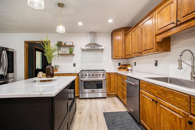 kitchen featuring brown cabinets, light wood finished floors, stainless steel appliances, a sink, and wall chimney exhaust hood