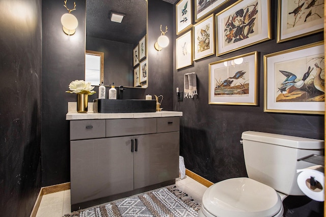 bathroom with a textured ceiling, toilet, vanity, baseboards, and tile patterned floors