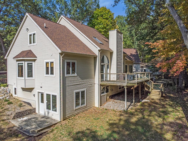 rear view of house with a chimney, a deck, a lawn, and roof with shingles