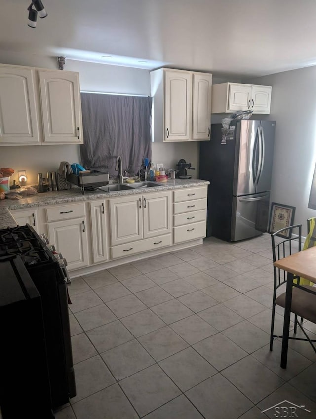 kitchen with stove, a sink, freestanding refrigerator, and white cabinets