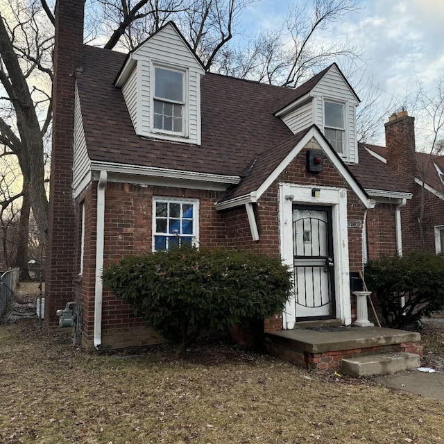 view of front of house featuring roof with shingles, a chimney, and brick siding