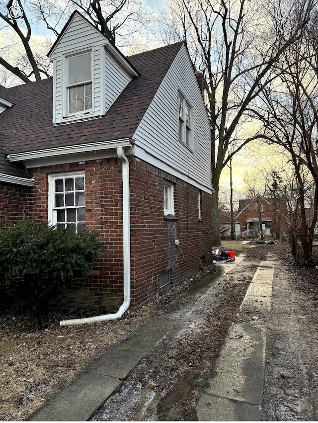 view of home's exterior featuring brick siding and a shingled roof