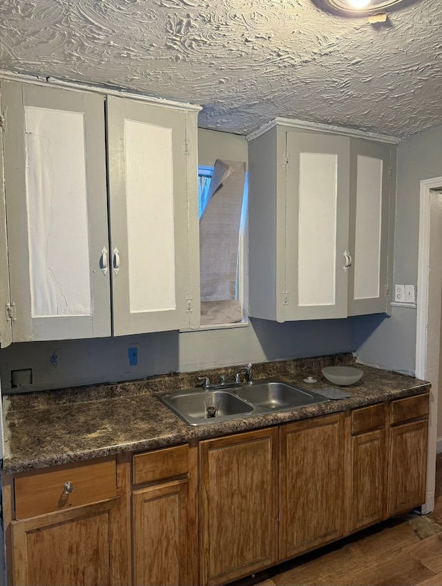 kitchen featuring white cabinets, dark countertops, brown cabinets, wood finished floors, and a sink