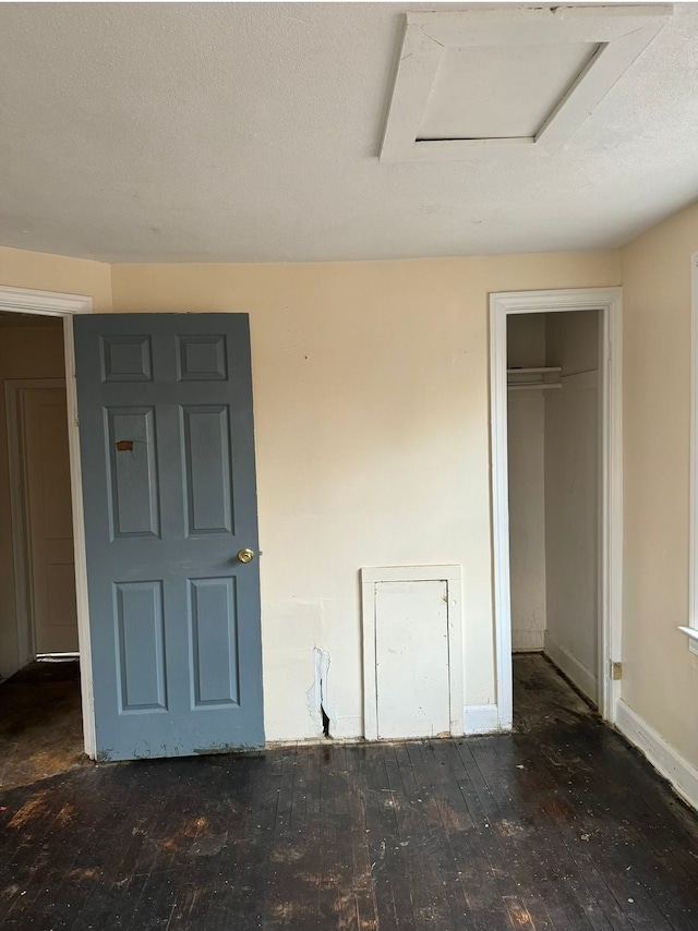 unfurnished bedroom featuring attic access, a textured ceiling, baseboards, and hardwood / wood-style flooring