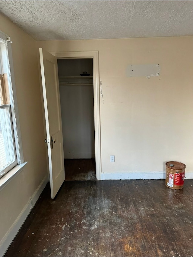 unfurnished bedroom featuring a textured ceiling, a closet, wood-type flooring, and baseboards