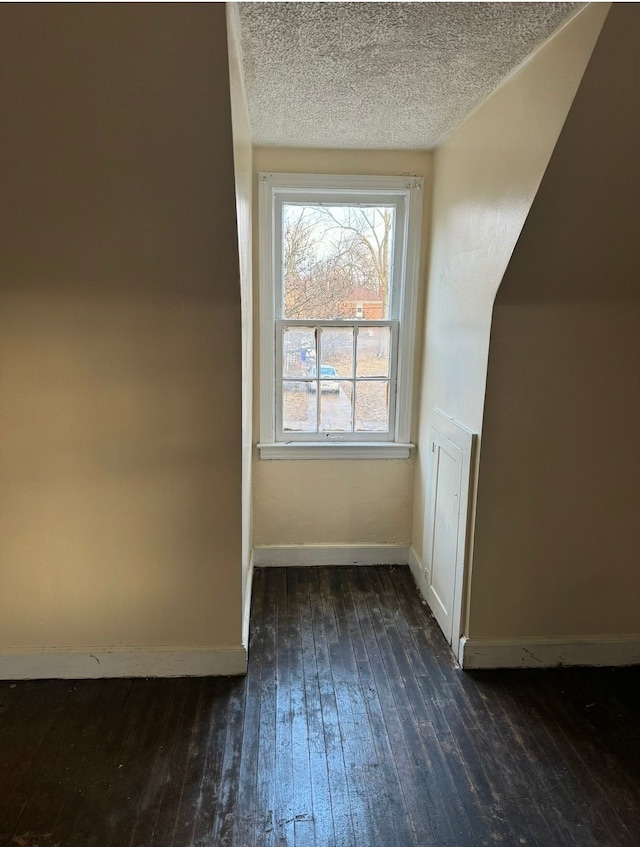 additional living space featuring baseboards, dark wood-type flooring, and a textured ceiling