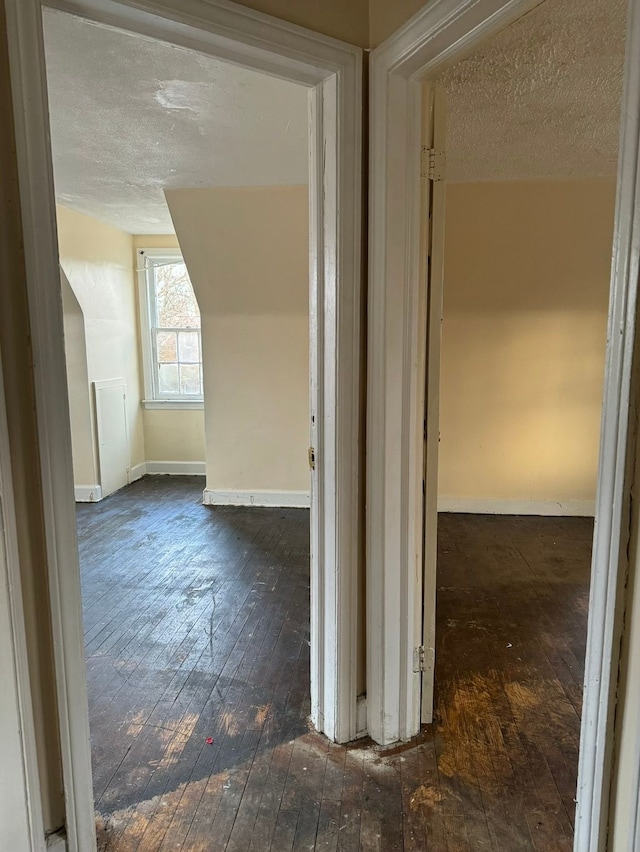 hall with lofted ceiling, hardwood / wood-style flooring, baseboards, and a textured ceiling