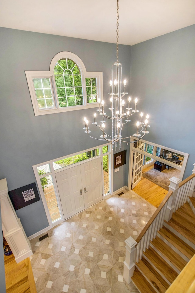 entrance foyer with a chandelier, visible vents, stairway, and a high ceiling