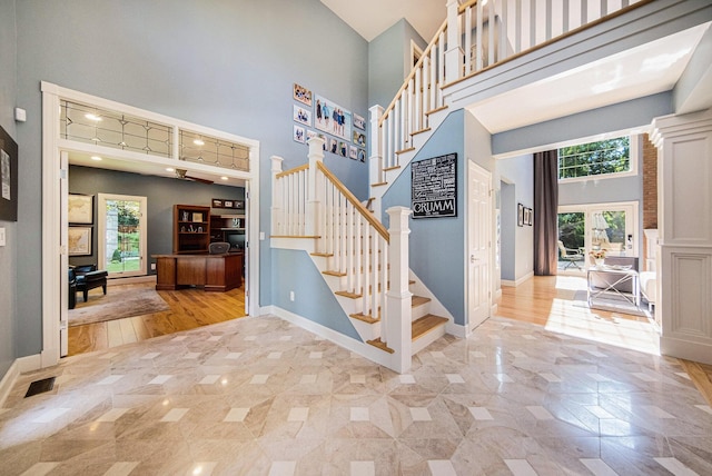 stairs with baseboards, visible vents, a towering ceiling, and a healthy amount of sunlight