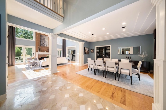 dining area featuring a fireplace, decorative columns, a raised ceiling, a towering ceiling, and wood finished floors