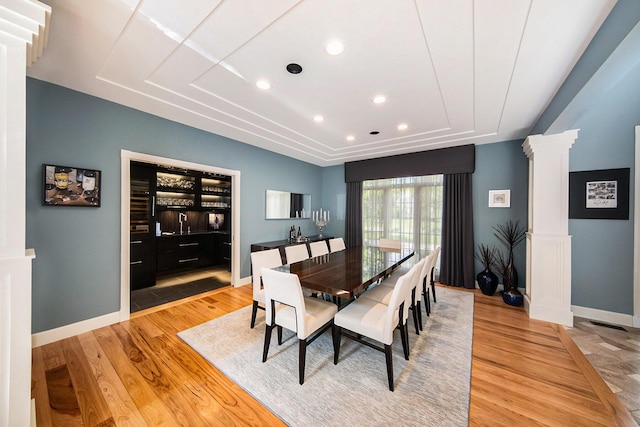 dining room with light wood-style floors, decorative columns, and baseboards