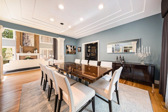 dining area featuring a tray ceiling, decorative columns, light wood finished floors, and recessed lighting