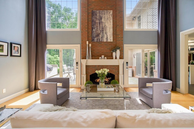 living area with a high ceiling, a brick fireplace, wood finished floors, and baseboards