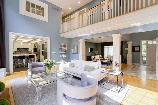 living area with a wealth of natural light, visible vents, decorative columns, and wood finished floors