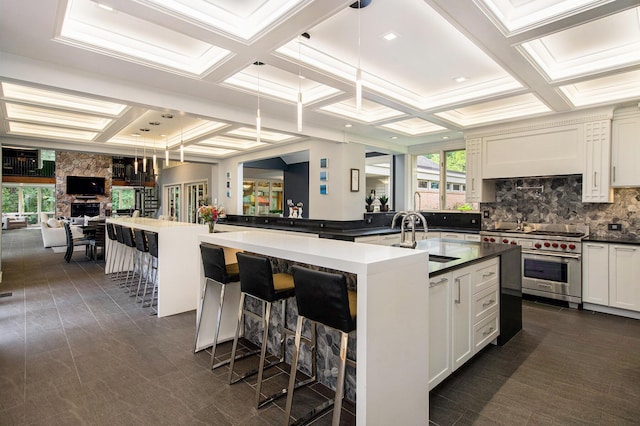 kitchen featuring a large island with sink, coffered ceiling, premium range, and a sink